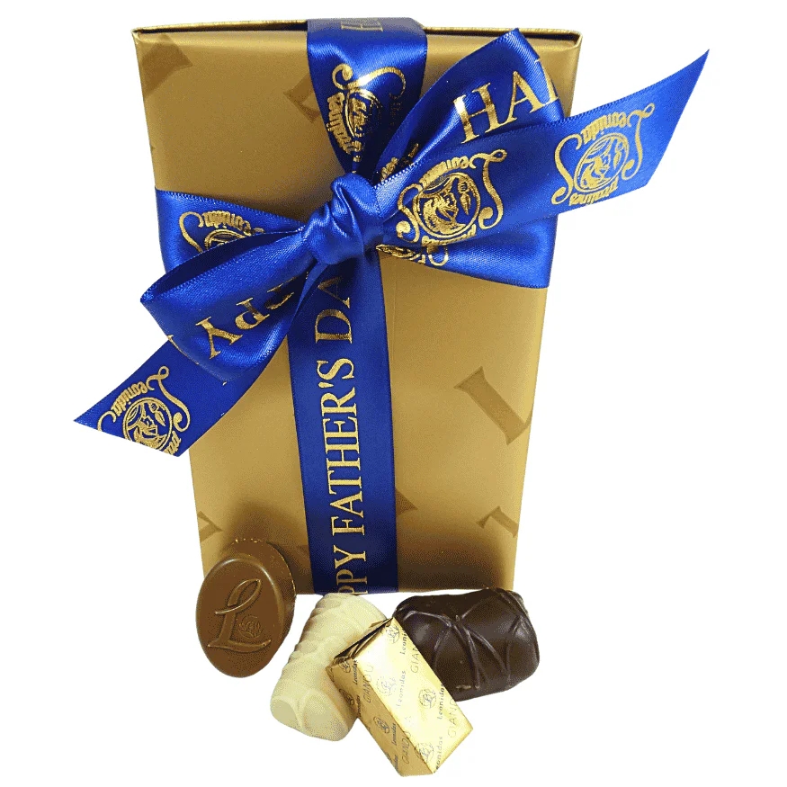 gold box of leonidas chocolates wrapped with a fathers day ribbon with chocolates in front